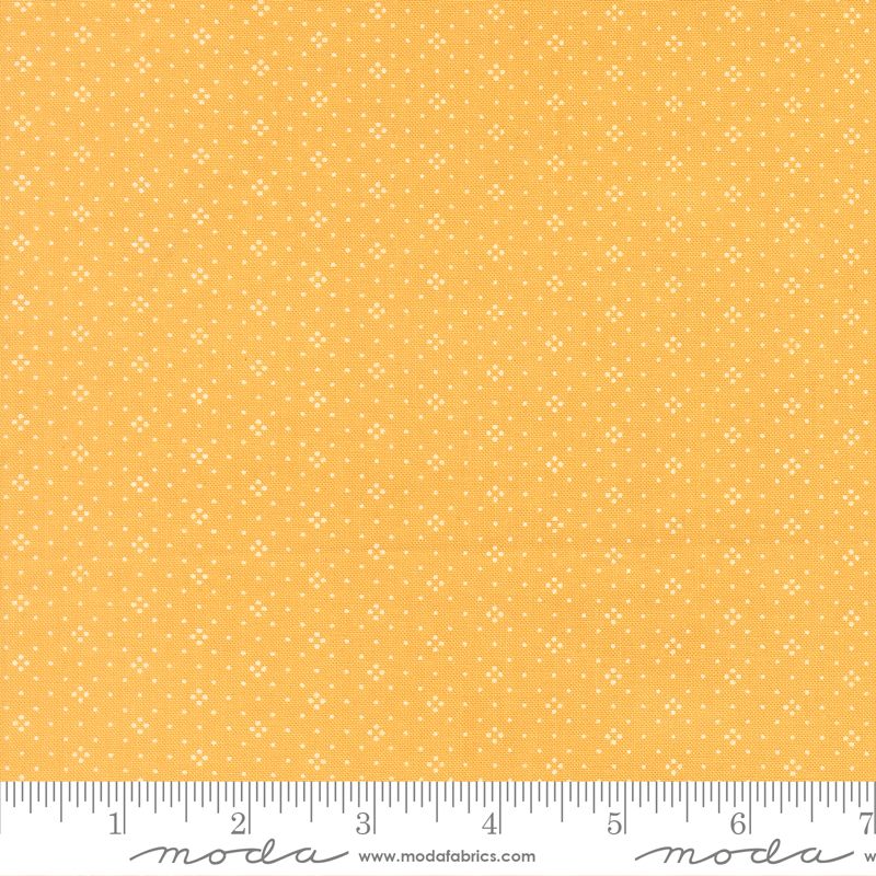 Yellow fabric with a small white geometric pattern, shown with a ruler at the bottom to indicate scale. The brand name 'Moda Fabrics' is visible at the bottom.