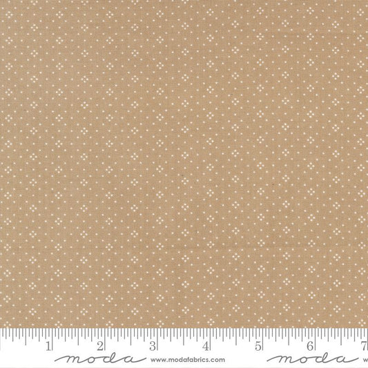 A close-up of a fabric pattern showing a warm tan/beige background with a repeating small white geometric dot motif. A ruler along the bottom edge shows the scale of the pattern repeat, and the brand name 'moda' with 'www.