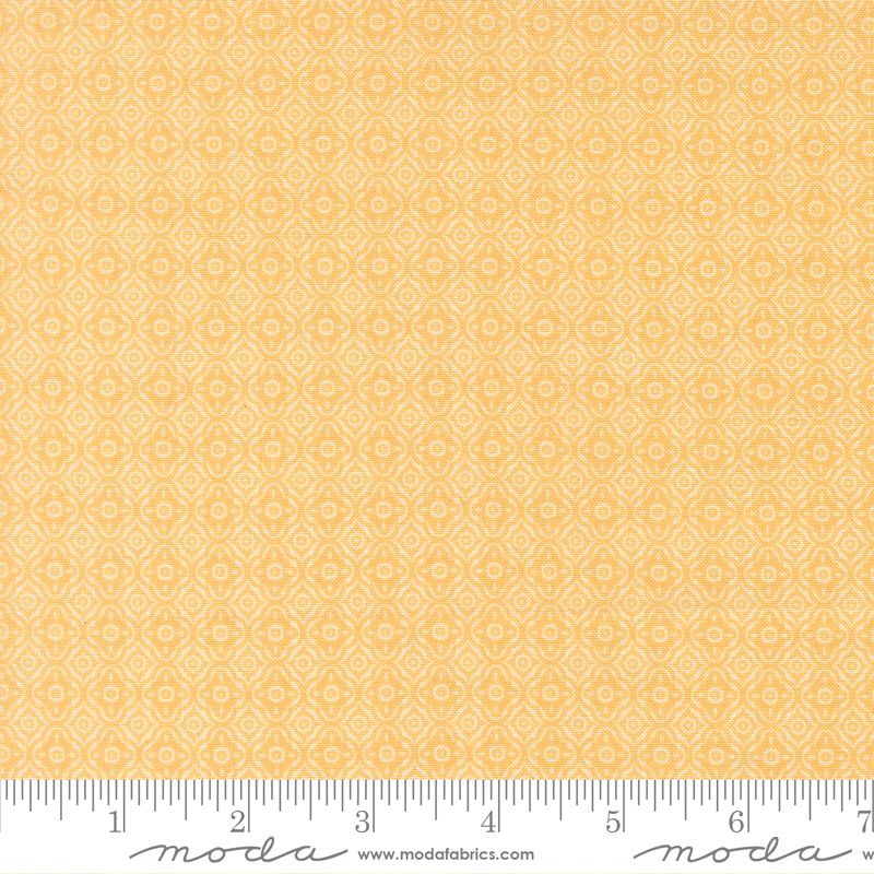 A close-up of a fabric pattern swatch in warm yellow-orange with a repeating small geometric diamond motif. A ruler and Modla watermark are visible along the bottom edge.