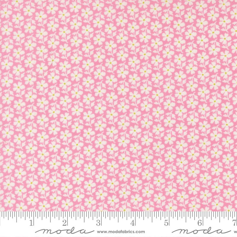 Pink fabric with a repeating white and yellow floral pattern, shown flat with a ruler along the bottom edge and Moda Fabrics branding.