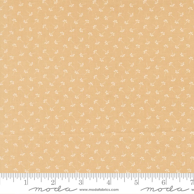 A close-up of a fabric pattern showing a warm tan-beige background with a repeating small white floral and vine motif, with a measuring ruler along the bottom edge for scale. The brand name 'moda fabrics' is visible on the ruler.