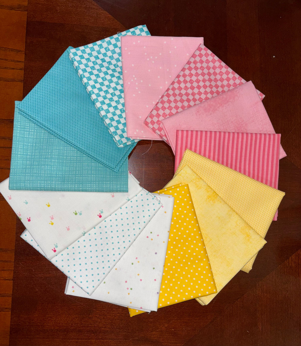 A circular arrangement of colorful fabric swatches with various patterns including stripes, polka dots, and checks, displayed on a dark wooden table.
