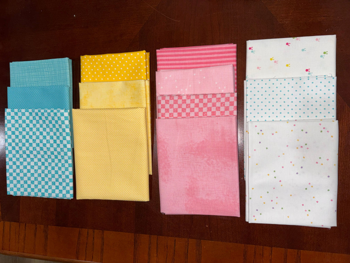 Four stacks of folded fabric swatches in blue, yellow, pink, and white patterns, arranged on a dark wooden table.
