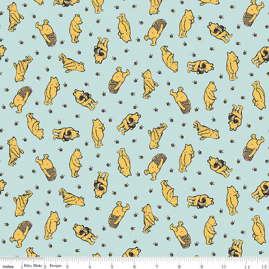 A repeating fabric pattern featuring Winnie the Pooh characters in yellow with bees on on a light blue background, with a small ruler at the bottom showing measurements.