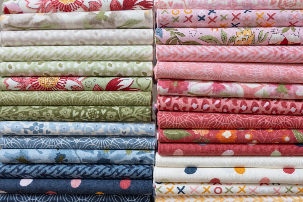 Two stacks of folded patterned fabric in various colors and designs, including floral, geometric, and polka dot prints, arranged side by side.