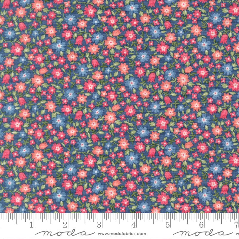 A close-up of a floral fabric pattern with small pink, red, and blue flowers, green leaves, and a dark blue background, shown with a measuring ruler along the bottom edge. The brand name 'moda' is visible on the ruler watermark.