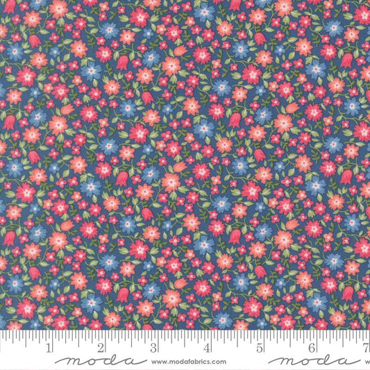 A close-up of a floral fabric pattern with small pink, red, and blue flowers, green leaves, and a dark blue background, shown with a measuring ruler along the bottom edge. The brand name 'moda' is visible on the ruler watermark.