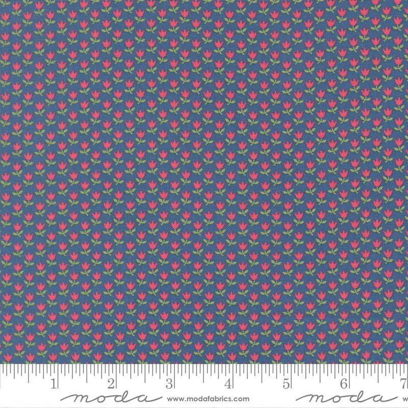 A close-up of a fabric pattern featuring small pink tulips with green leaves on a slate blue background, with a measuring ruler along the bottom edge showing scale. The brand name 'Moda Fabrics' is visible on the ruler.