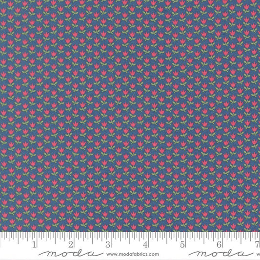 A close-up of a fabric pattern featuring small pink tulips with green leaves on a slate blue background, with a measuring ruler along the bottom edge showing scale. The brand name 'Moda Fabrics' is visible on the ruler.