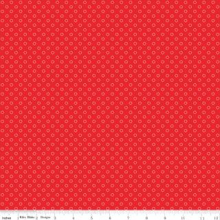 Red fabric with a repeating small white circular pattern, shown flat with a ruler along the bottom edge for scale.
