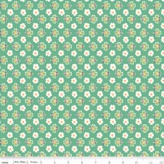 A close-up of a fabric pattern featuring a repeating design of white daisies and green clovers on a light green background, with a white ruler visible along the bottom edge.