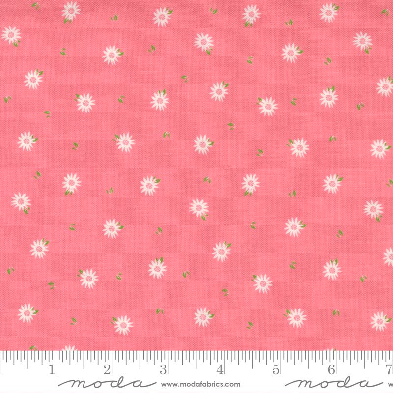 Pink fabric with a repeating pattern of small white daisy-like flowers and tiny green leaves, shown flat with a ruler along the bottom edge for scale. The brand name Modas Fabrics is visible in script on the ruler.