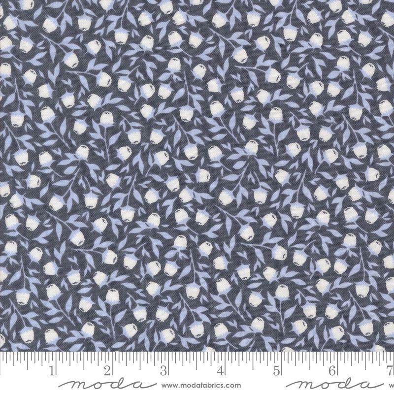 A close-up of a fabric pattern featuring small white flowers and light blue leaves on a navy background, with a ruler along the bottom edge and Moda branding at the bottom.