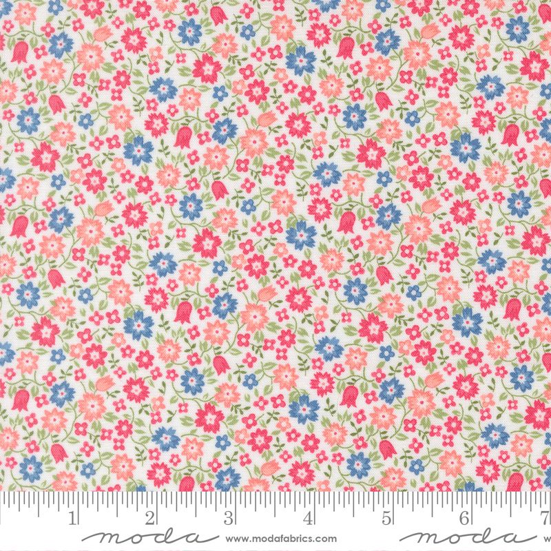 A close-up of a floral fabric pattern with small pink, blue, and coral flowers and green leaves on a light cream background, with a ruler along the bottom edge showing scale. The word 'moda' appears at the bottom.