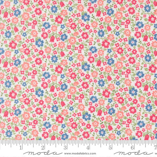 A close-up of a floral fabric pattern with small pink, blue, and coral flowers and green leaves on a light cream background, with a ruler along the bottom edge showing scale. The word 'moda' appears at the bottom.