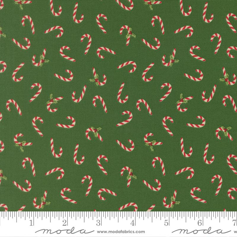 Green fabric with a repeating pattern of red and white striped candy canes and small green holly leaves, shown with a ruler along the bottom edge.