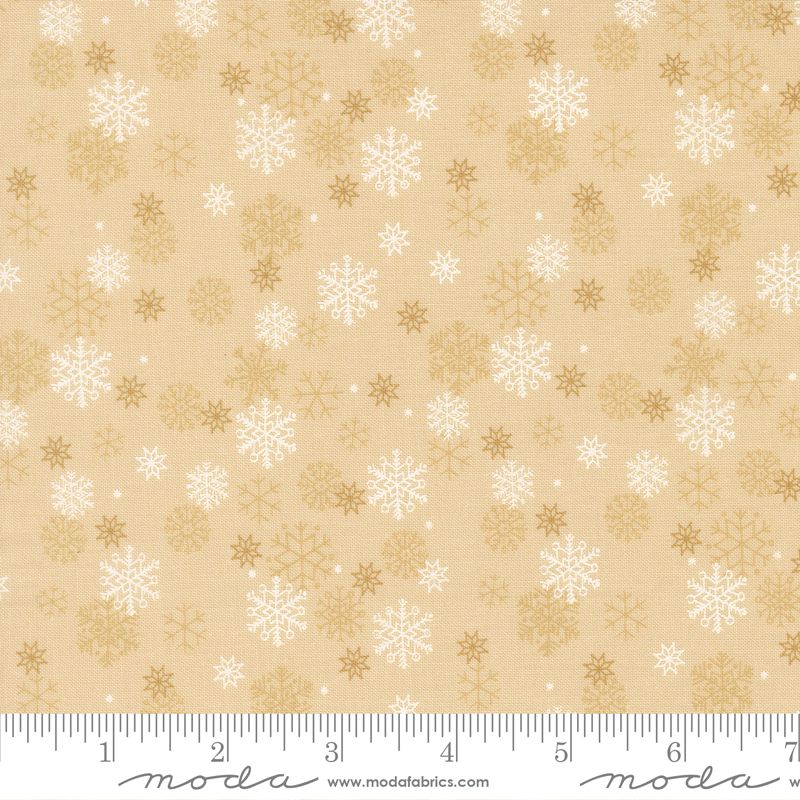 A close-up of a fabric pattern featuring white and tan snowflakes on a warm beige background, with a measuring ruler along the bottom edge showing the scale.