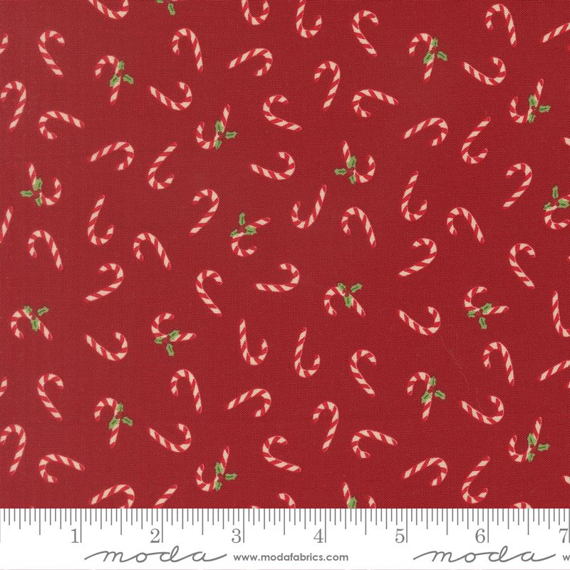 Red fabric with a repeating pattern of white and pink striped candy canes and small green holly leaves, shown with a white ruler along the bottom edge.
