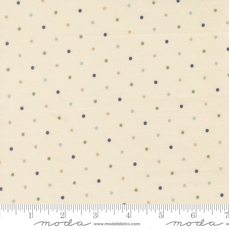 A close-up of a fabric pattern featuring small scattered polka dots in navy, olive green, and tan on a warm cream background, with a ruler along the bottom edge showing measurement scale and Modra branding.