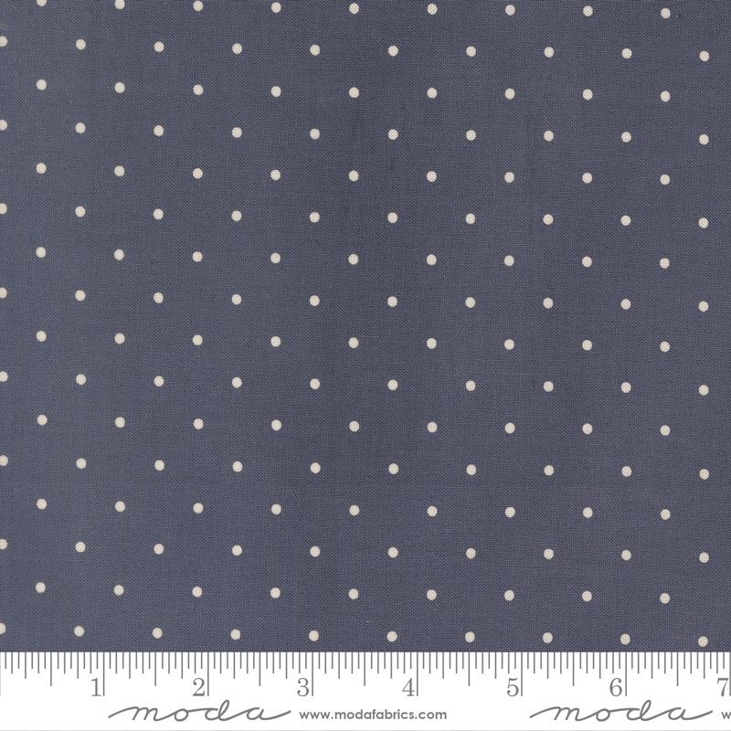 A close-up of a fabric pattern featuring small, evenly spaced cream-colored polka dots on a dark slate blue background, with a white ruler at the bottom showing scale.