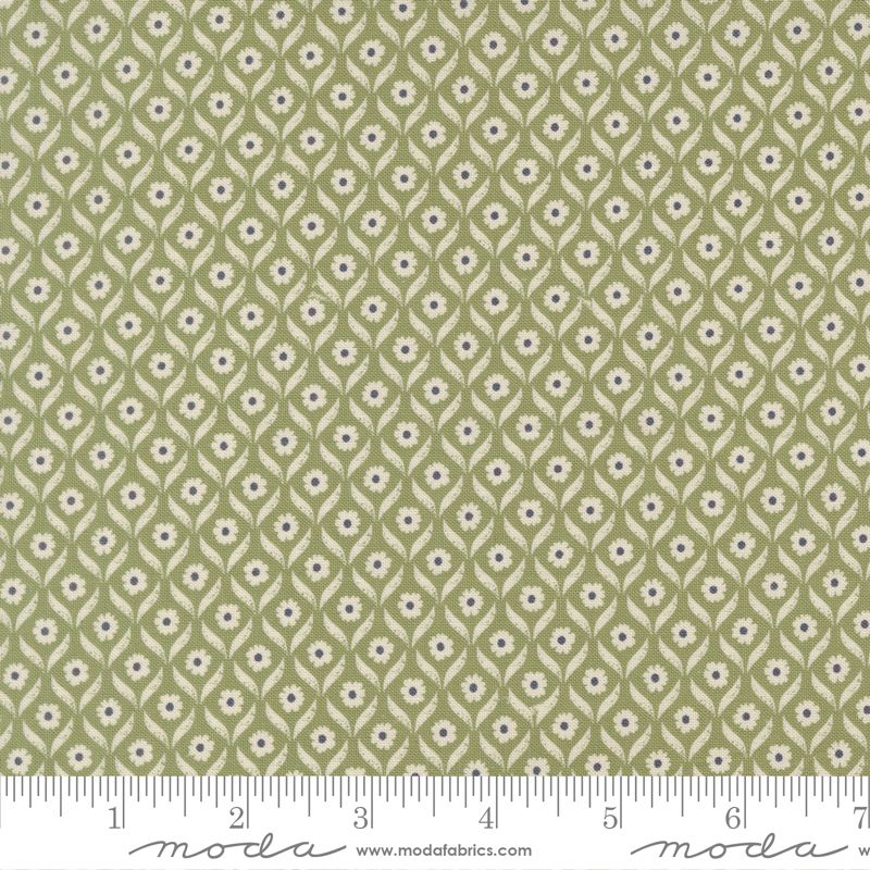 A close-up of a fabric pattern with a sage green background, featuring a repeating geometric leaf and flower motif in cream and blue. A white ruler with black markings is visible along the bottom edge, and the Moda Fabrics logo is printed on the white border at the bottom.