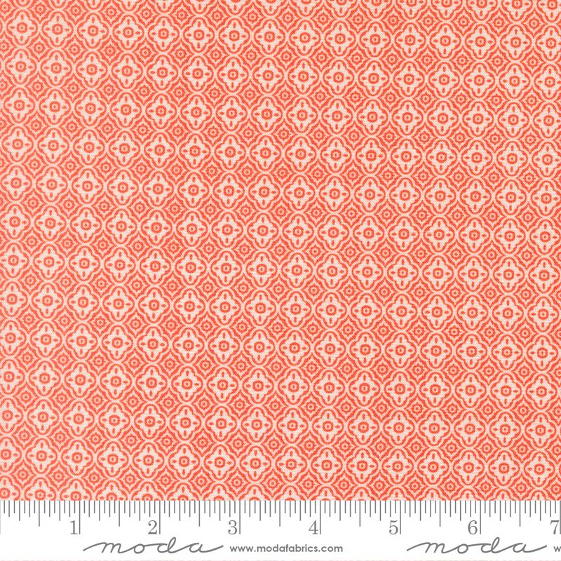 A close-up of a fabric pattern swatch featuring a repeating coral orange and white geometric medallion design, with a measuring ruler along the bottom edge for scale. The brand name 'Moda Fabrics' is visible at the bottom.