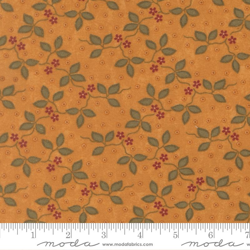 A close-up of a fabric pattern featuring green leaves and small red flowers on a warm orange-brown background, with a white ruler along the bottom edge showing measurement markings and a Modas fabric watermark.