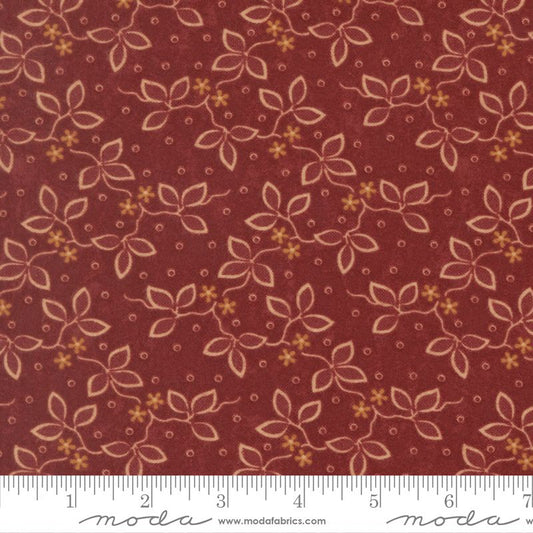 A close-up of a fabric pattern featuring a repeating floral vine design in beige and mustard yellow on a deep reddish-brown background, with a white ruler strip along the bottom edge showing measurements.