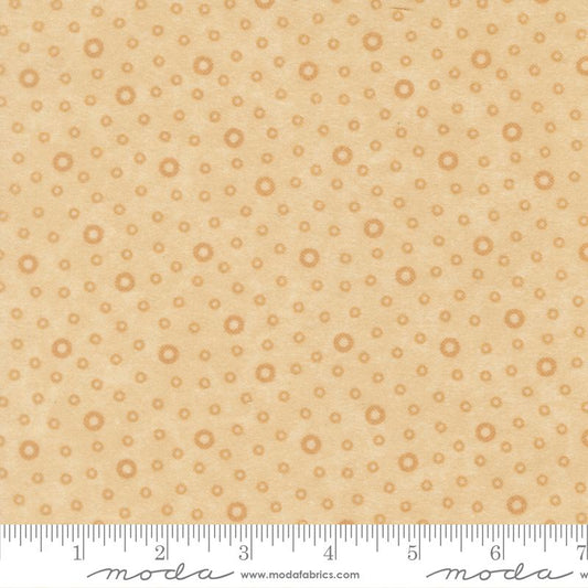 A close-up of a fabric pattern featuring small tan circular motifs on a warm beige background, with a ruler along the bottom edge showing scale and Modas Fabrics branding.