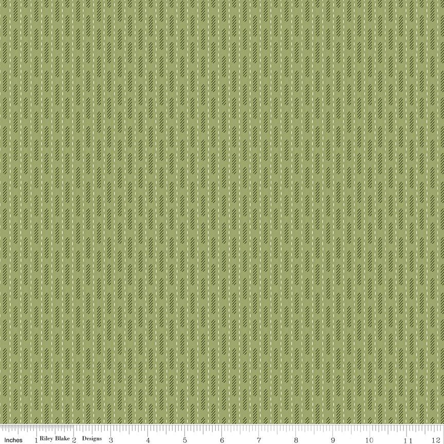 A close-up fabric pattern swatch showing a repeating vertical stripe design in muted olive green and sage, with a ruler scale along the bottom edge indicating inches and the brand Riley Blake Designs.