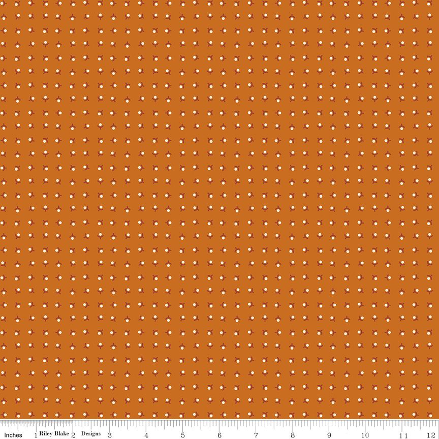 A close-up fabric pattern swatch showing an orange background with a repeating grid of small white dots. A white ruler along the bottom edge includes the text 'Riley Blake Designs' and inch markings, indicating the brand and scale.