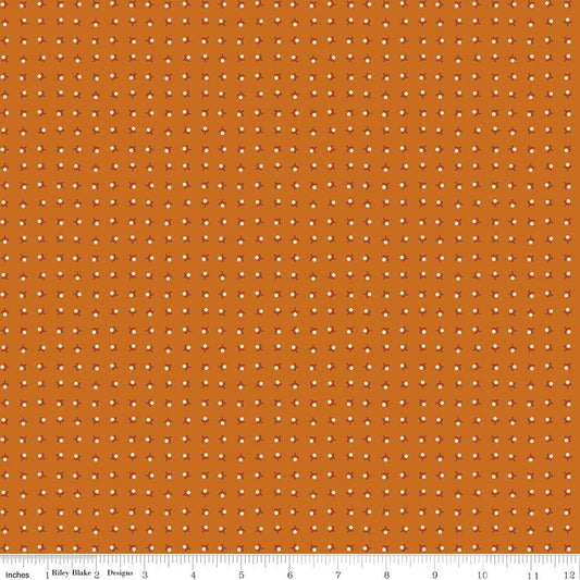 A close-up fabric pattern swatch showing an orange background with a repeating grid of small white dots. A white ruler along the bottom edge includes the text 'Riley Blake Designs' and inch markings, indicating the brand and scale.