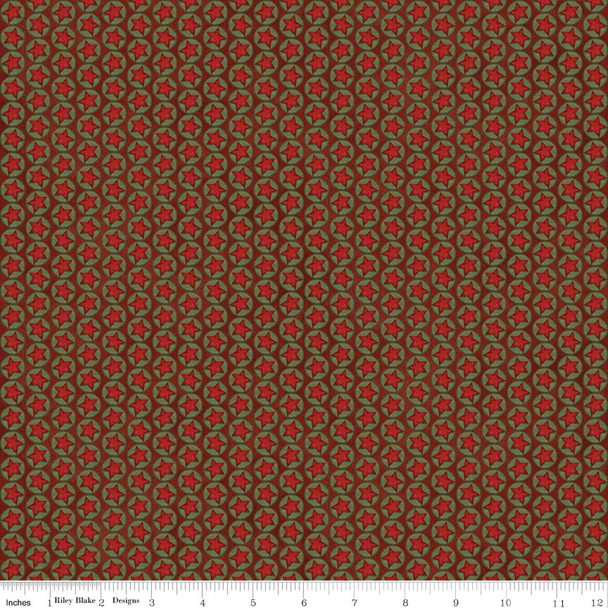 A close-up of a fabric pattern showing a repeating design of red five-pointed stars enclosed in curved olive-green leaf-like loops over a dark brown background. A white ruler at the bottom edge displays the scale with inch markings and the text 'Riley Blake Designs'.