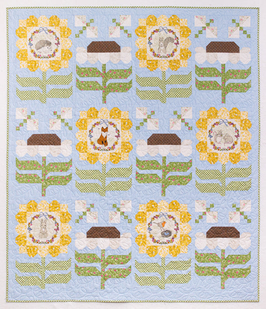 A square quilt featuring a repeating floral and animal motif on a light blue background. The design includes yellow flowers with white centers, white blossoms with green stems, and circular motifs containing small animals, a hedgehog, squirrel, fox, mice, rabbit, and birds.
