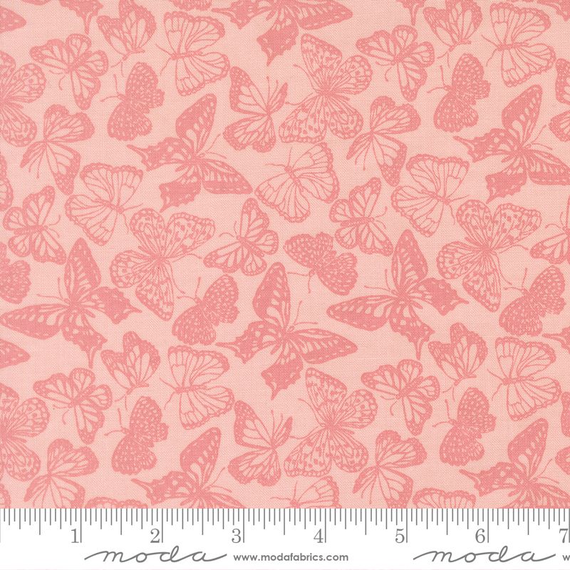 A close-up of a fabric pattern featuring pink butterflies on a light peach-pink background, with a measuring ruler along the bottom edge and Modas Fabrics branding at the bottom.