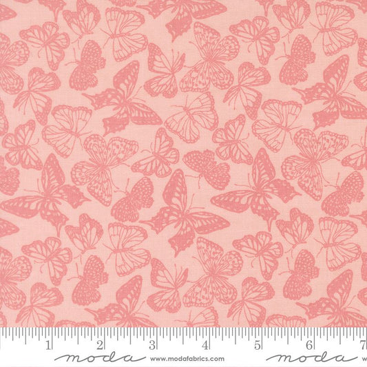 A close-up of a fabric pattern featuring pink butterflies on a light peach-pink background, with a measuring ruler along the bottom edge and Modas Fabrics branding at the bottom.