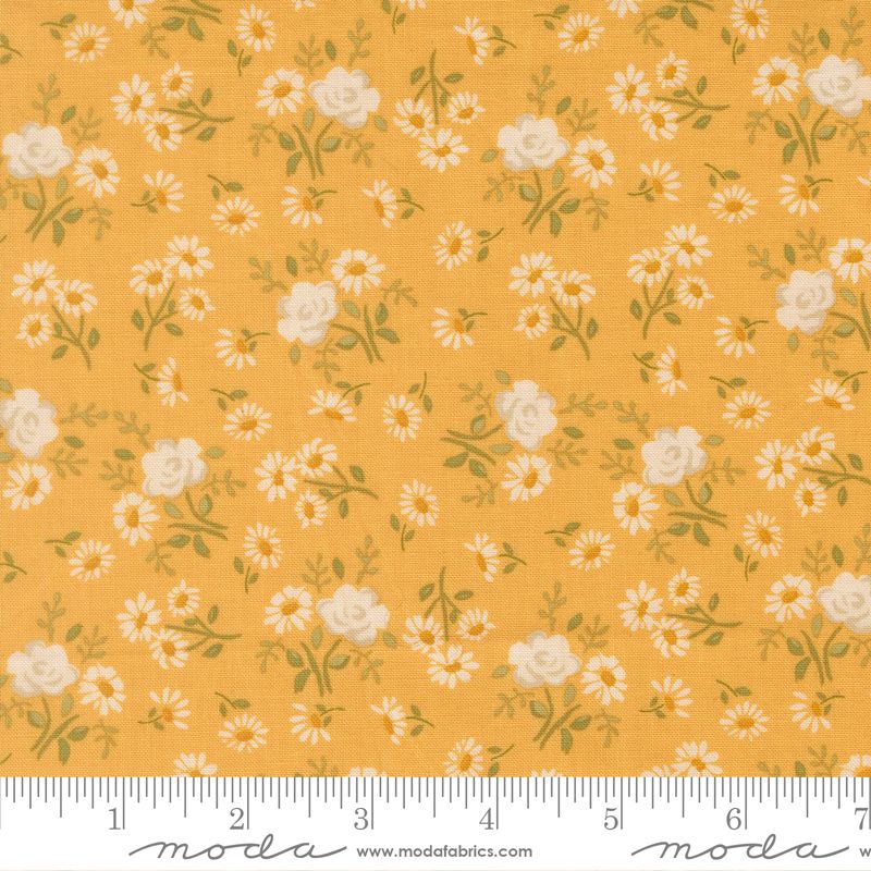 A close-up of a fabric pattern featuring small white daisies and larger cream roses with green leaves on a warm mustard-yellow background. A white ruler along the bottom edge shows the scale of the print, and the Modas Fabrics logo is visible at the bottom.