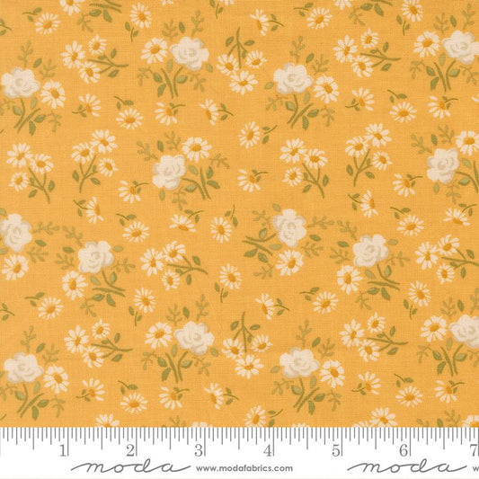 A close-up of a fabric pattern featuring small white daisies and larger cream roses with green leaves on a warm mustard-yellow background. A white ruler along the bottom edge shows the scale of the print, and the Modas Fabrics logo is visible at the bottom.
