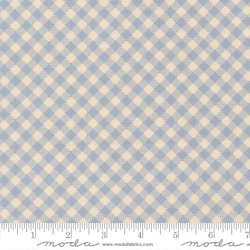 A close-up of a fabric pattern showing a light blue and cream gingham check design, with a measuring ruler along the bottom edge for scale. The brand name 'Moda Fabrics' is visible at the bottom.