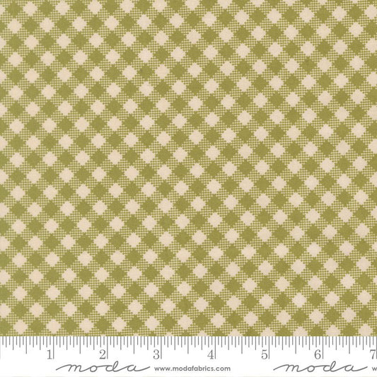 A close-up of a fabric pattern with an olive green and cream gingham-style check design, shown with a ruler along the bottom edge for scale. The brand name 'moda' and website 'www.