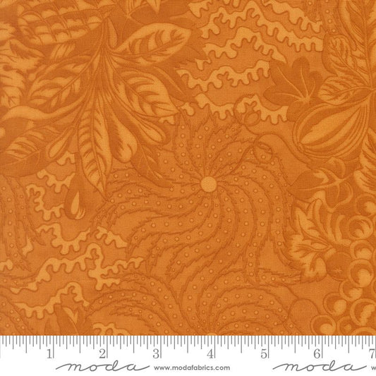 A close-up of butterscotch fabric with a floral and leaf pattern, shown with a measuring ruler along the bottom edge. The brand name 'Moda' is visible on the ruler.