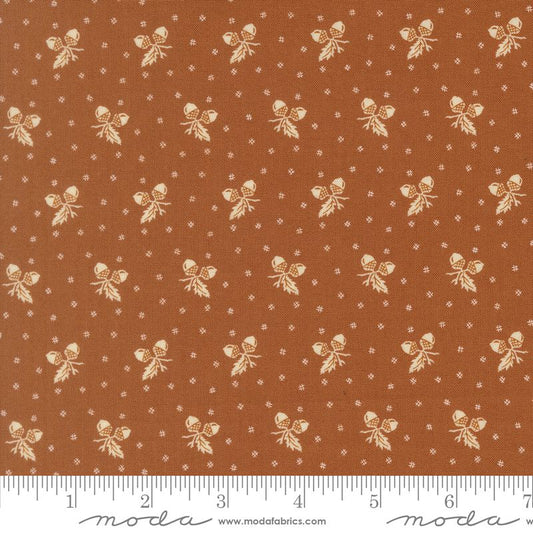 A close-up of a fabric pattern featuring a warm rust-orange background with a repeating cream acorn and leaf motif, small white dotted diamond motifs, and a white ruler along the bottom edge showing measurements. The brand name 'moda' is visible on the ruler watermark.