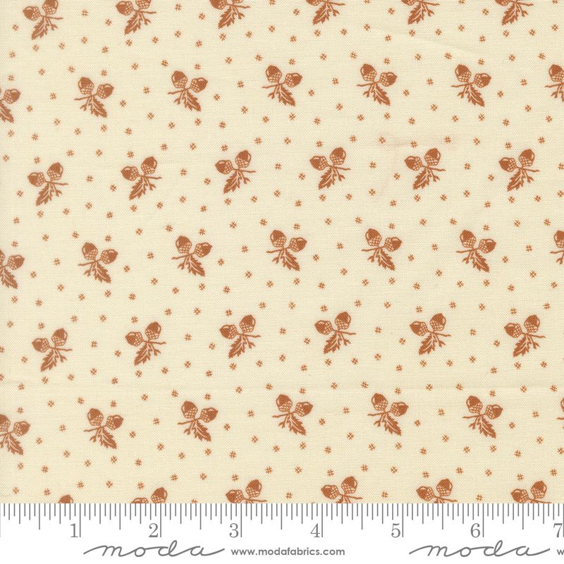 A close-up of a fabric pattern featuring a repeating motif of small brown acorn sprigs and tiny brown dots on a warm cream background, with a measuring ruler along the bottom edge showing the scale.