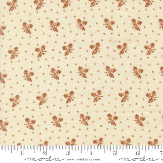 A close-up of a fabric pattern featuring a repeating motif of small brown acorn sprigs and tiny brown dots on a warm cream background, with a measuring ruler along the bottom edge showing the scale.