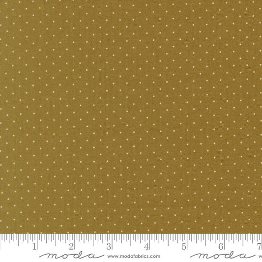 A close-up of a fabric pattern featuring small white polka dots on a warm olive background, with a white ruler along the bottom edge showing measurements and Moda Fabrics branding.