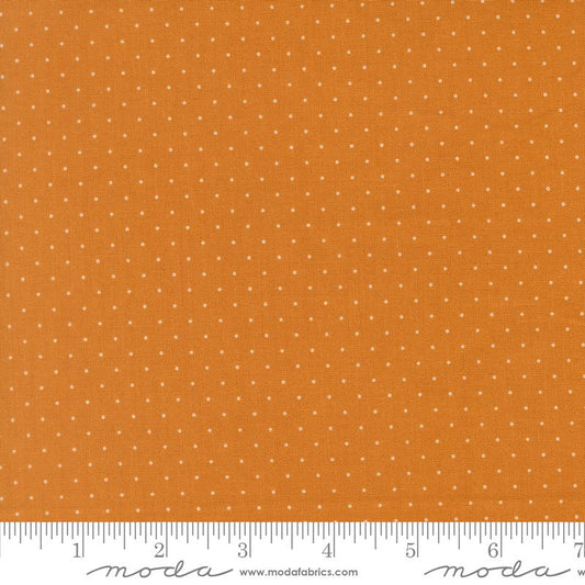 A close-up fabric swatch showing an orange background with a repeating pattern of small white dots. A white ruler along the bottom edge shows measurement markings, and the Moda Fabrics logo and website appear at the bottom.