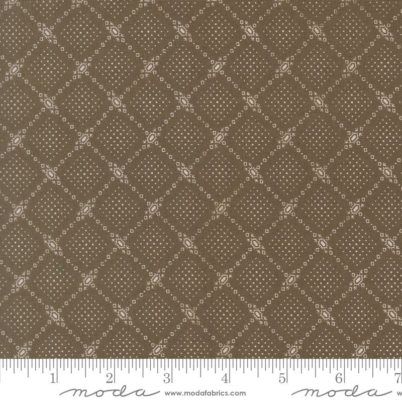 A close-up of a fabric pattern showing a repeating brown and beige diamond lattice design with small decorative motifs. A white ruler along the bottom edge shows measurement markings, and the brand name 'moda' with 'www.