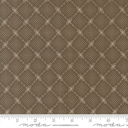 A close-up of a fabric pattern showing a repeating brown and beige diamond lattice design with small decorative motifs. A white ruler along the bottom edge shows measurement markings, and the brand name 'moda' with 'www.