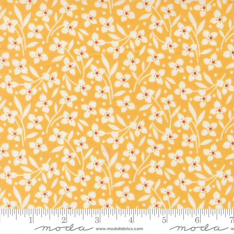 A close-up of a fabric pattern featuring small white flowers and leaves on a warm yellow-orange background, with a measuring ruler along the bottom edge and Modas Fabrics branding.