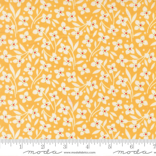 A close-up of a fabric pattern featuring small white flowers and leaves on a warm yellow-orange background, with a measuring ruler along the bottom edge and Modas Fabrics branding.
